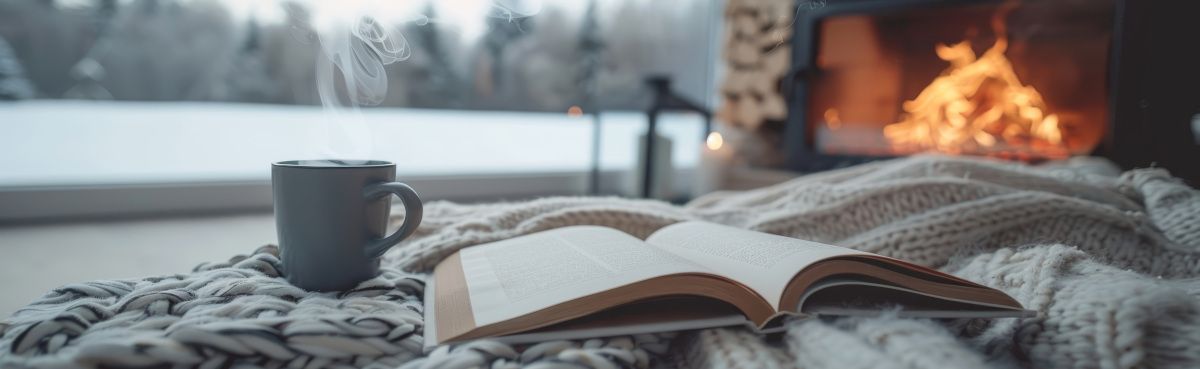 Cozy indoor winter scene with book and hot drink mug in front of a fireplace